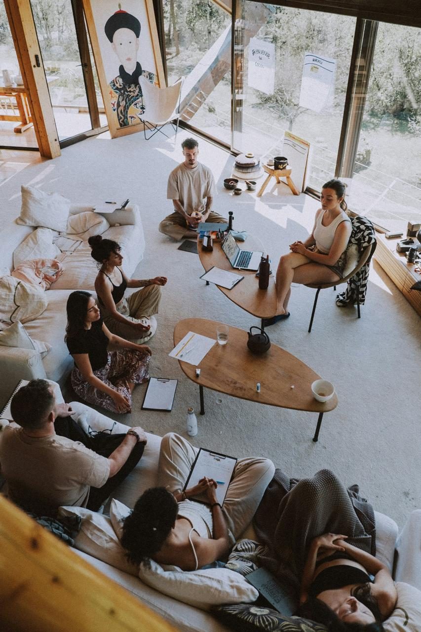 A circle of people seated on cushions in a bright room