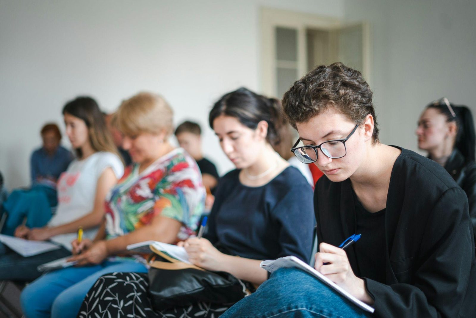 People seated in a row, taking notes during a class